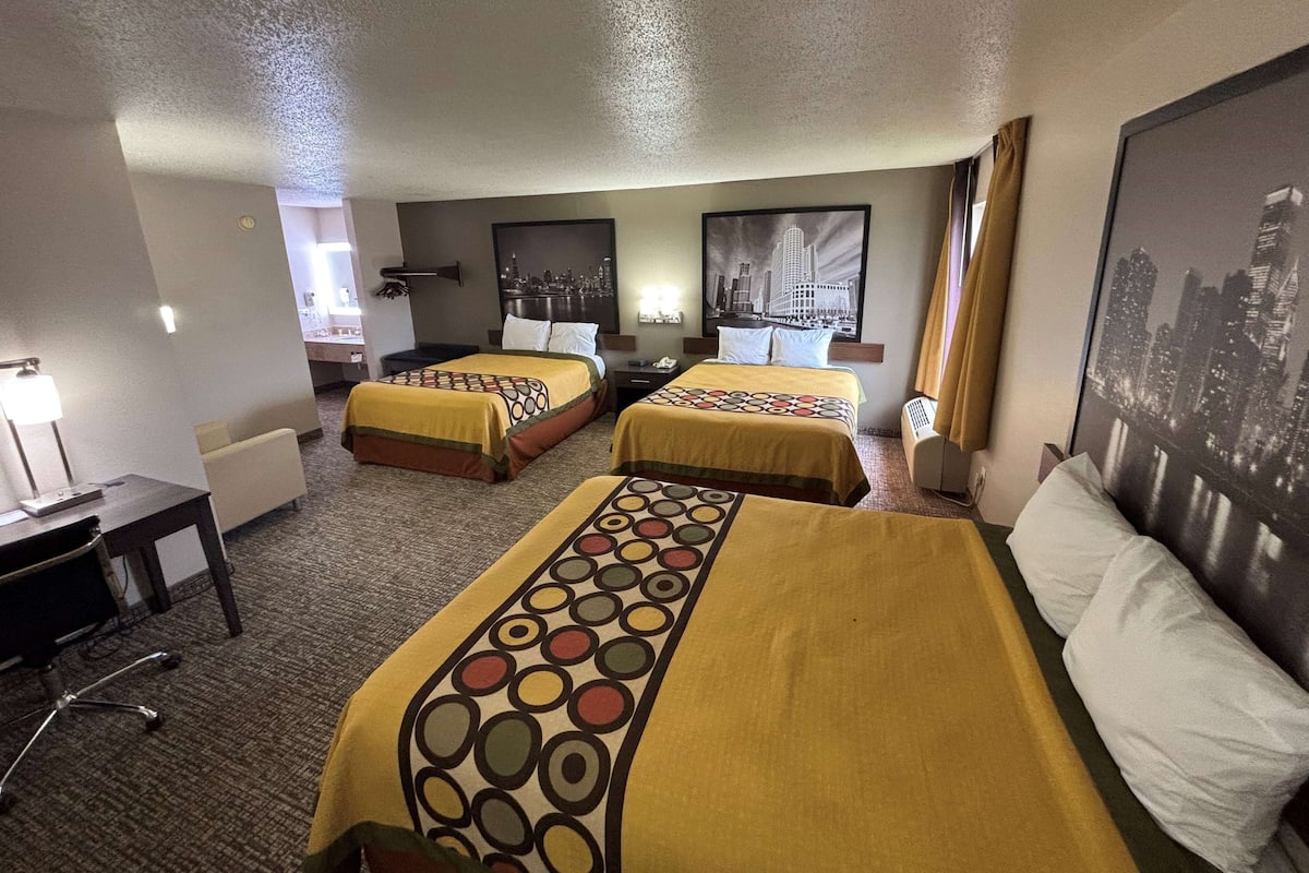 A hotel room with two beds, a desk, and a chair. There are two nightstands with lamps and a window with curtains.