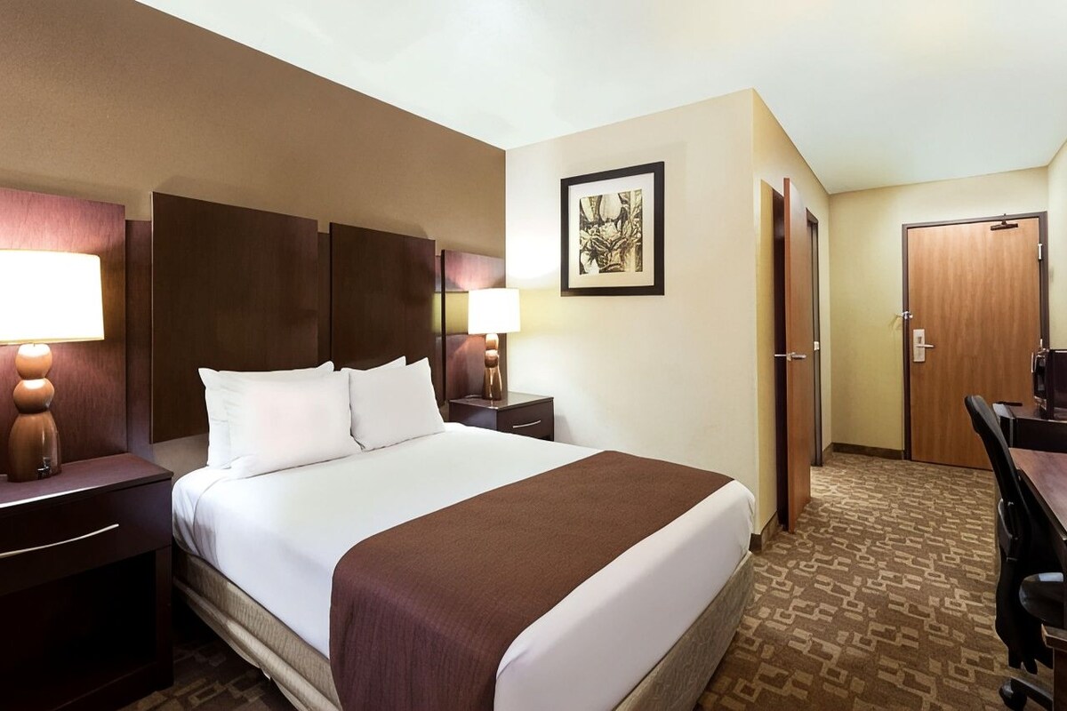 A hotel room with a large bed, two bedside tables with lamps, a framed artwork on the wall, and a door leading to another room.
