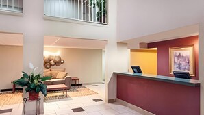 A hotel lobby with a reception desk, a seating area with a sofa and a coffee table, a potted plant, and a wall-mounted artwork. - Rodeway Inn & Suites Chandler - Phoenix South I-10 (Chandler)