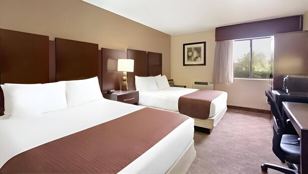 A hotel room with two beds, a desk, a chair, a lamp, and a window with a view. - Rodeway Inn & Suites Chandler - Phoenix South I-10 (Chandler)