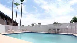 A swimming pool with lounge chairs and a fence, surrounded by tall palm trees and a building in the background. - Rodeway Inn & Suites Chandler - Phoenix South I-10 (Chandler)