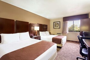 A hotel room with two beds, a desk, a chair, a lamp, and a window with curtains.