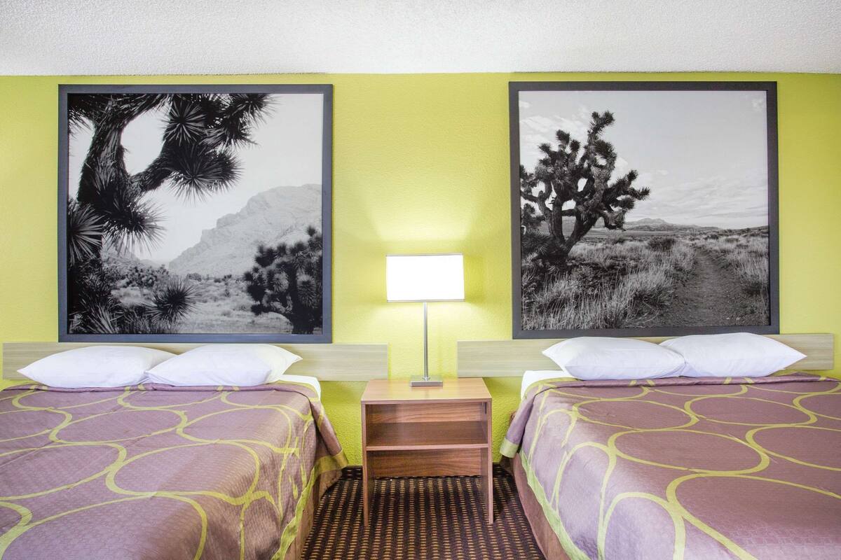 Een hotelkamer met twee bedden, een nachtkastje met een lamp en twee prenten van woestijnlandschappen aan de muur.