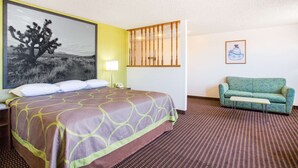 Una habitación de hotel con una cama, un sofá verde, un cuadro de un árbol en el desierto y una alfombra estampada.