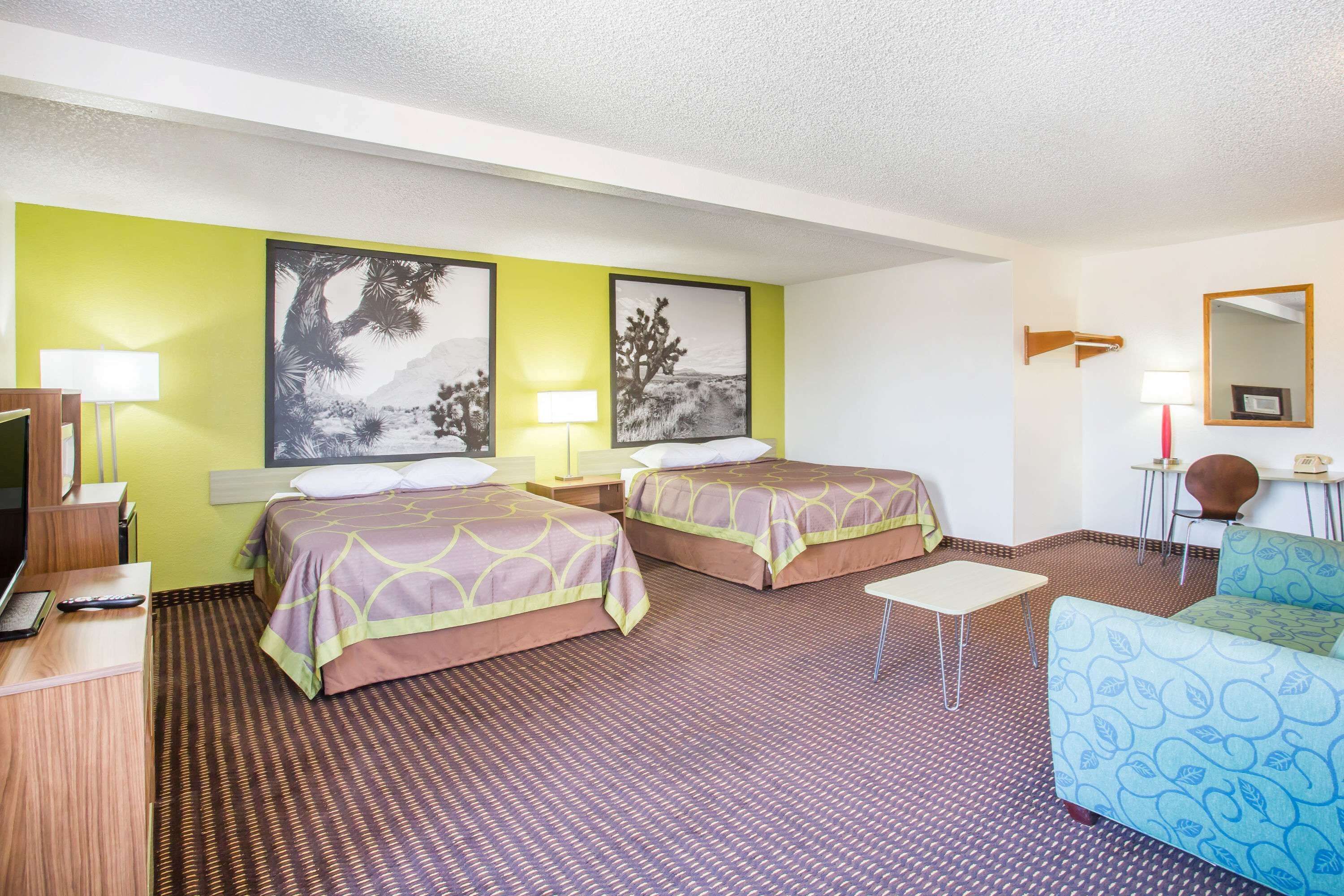 Una habitación de hotel con dos camas, un escritorio con computadora, una silla y una mesita.