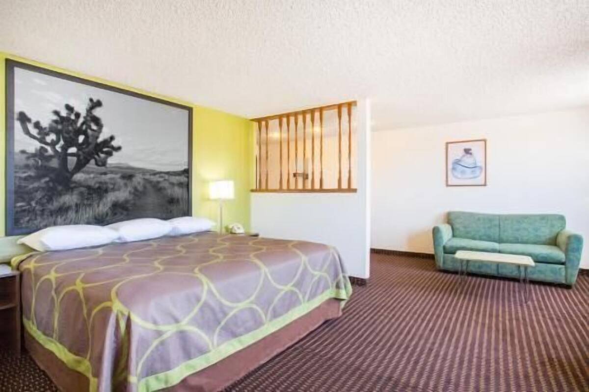 Een hotelkamer met een bed, een groene bank, een schilderij aan de muur en een lamp.