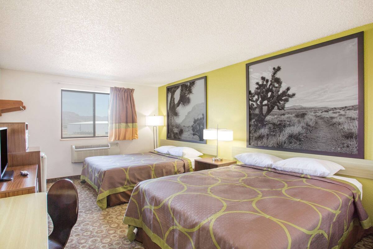 Een hotelkamer met twee bedden, een bureau met een computer, een stoel en een raam met gordijnen.