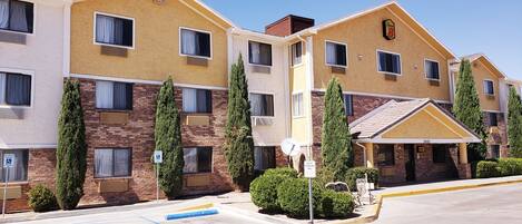 A multi-story hotel with a yellow and brown facade, multiple windows, and a guest parking area.