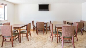 Un comedor con mesas y sillas de madera, un televisor de pantalla plana en la pared, y un ventanal que proporciona luz natural.