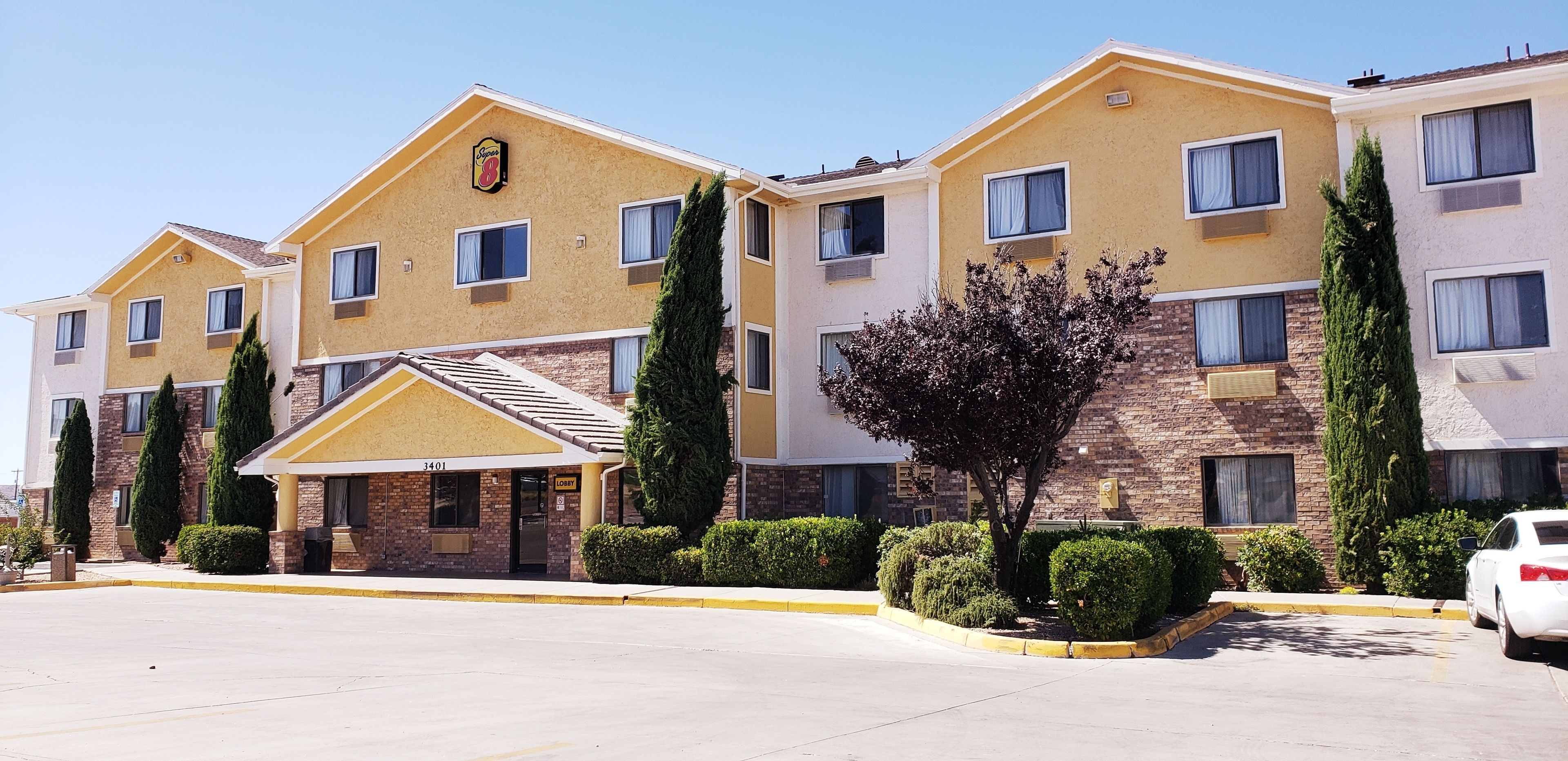 A multi-story hotel with a yellow facade, a lobby entrance, and a parking area.