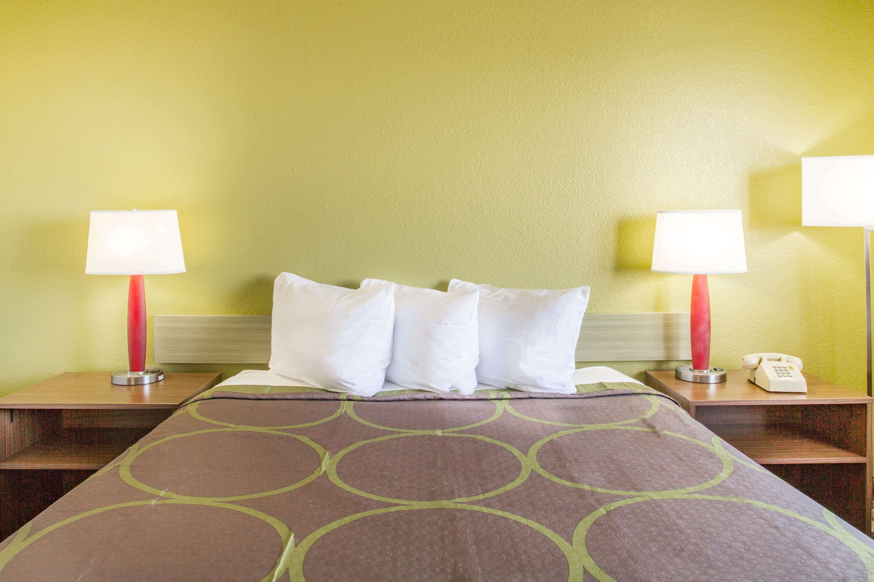 Una habitación de hotel con una cama, dos lámparas de noche, un teléfono y una mesita de noche.