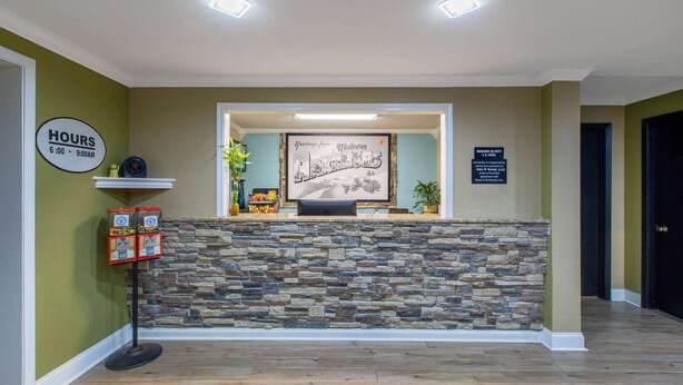 A reception area with a stone wall, a clock, a sign indicating hours, and a framed welcome sign.