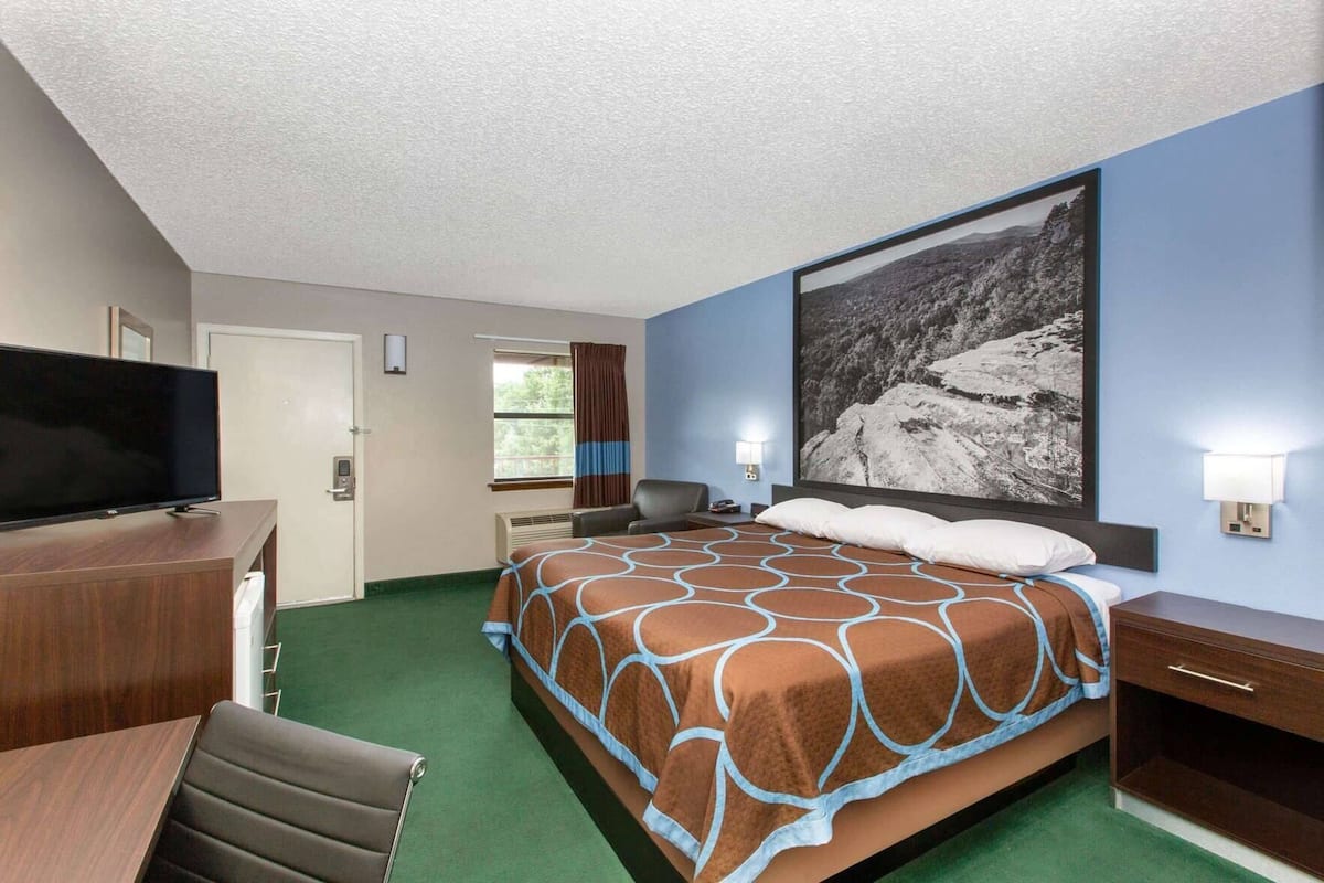 Une chambre d’hôtel comprenant un lit, un bureau avec une télévision, une chaise, une fenêtre avec des rideaux et une lampe fixée au mur.