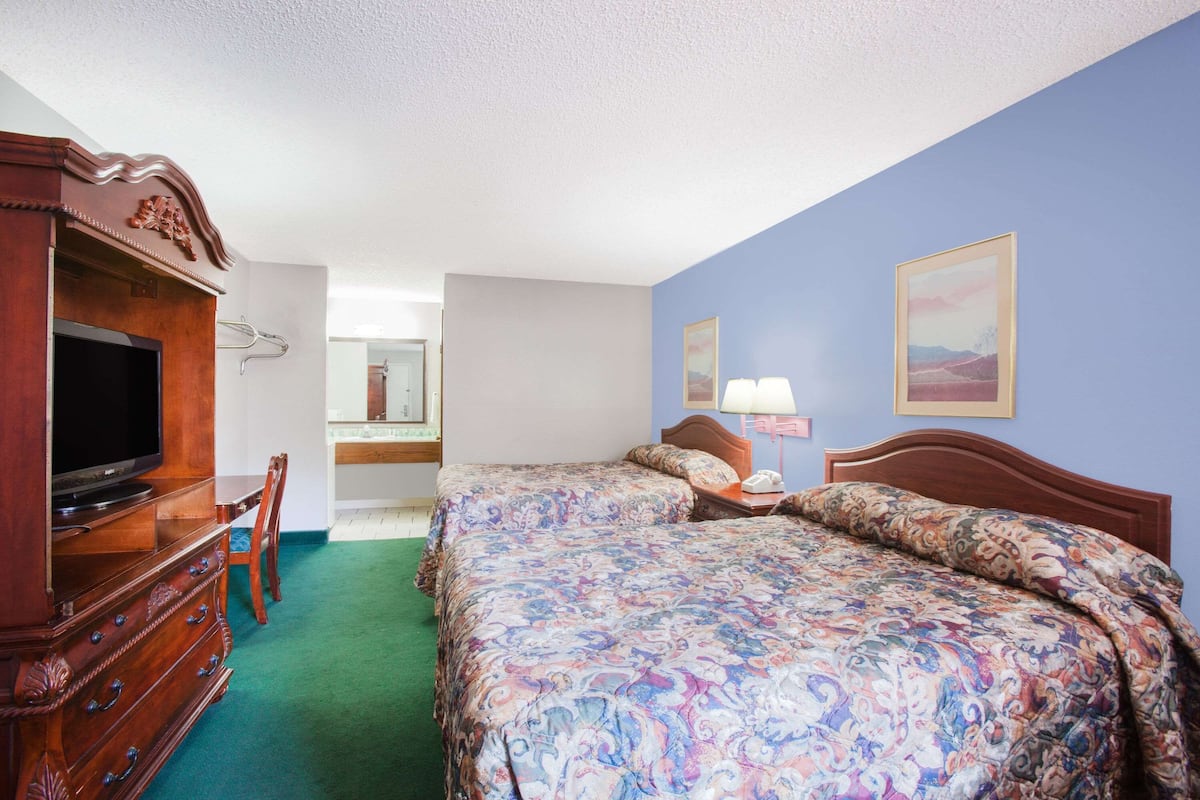 Une chambre d’hôtel avec un grand lit, une commode en bois sur laquelle se trouve un téléviseur, un bureau et une chaise. Il y a deux tableaux accrochés au mur.