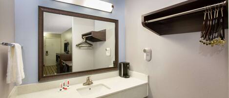 Une salle de bain avec un grand miroir, un lavabo, un porte-serviettes et une étagère sur laquelle sont suspendus divers objets.