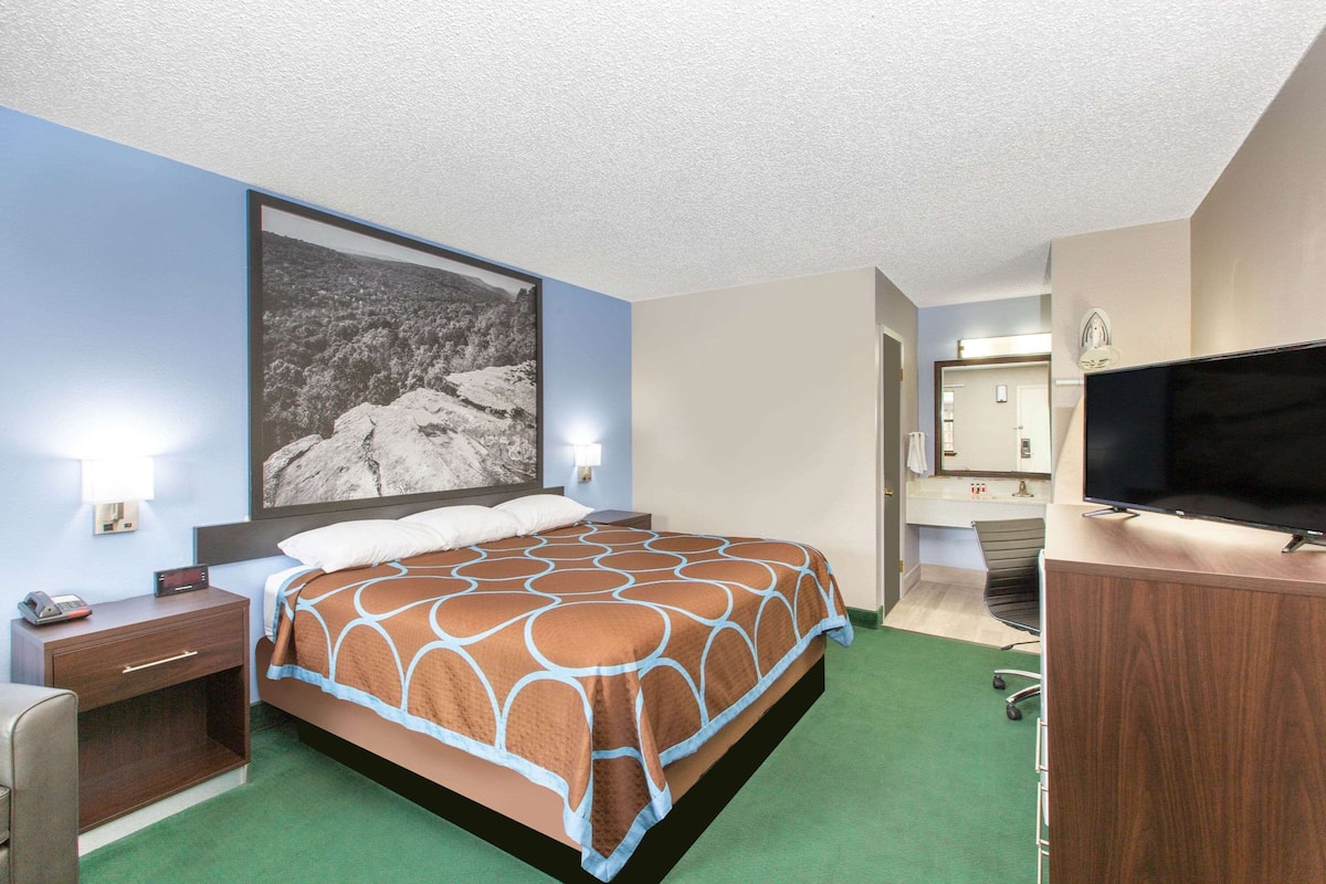 Une chambre d’hôtel avec un lit, un bureau, une chaise, une télévision et une salle de bain visible à travers une porte ouverte.