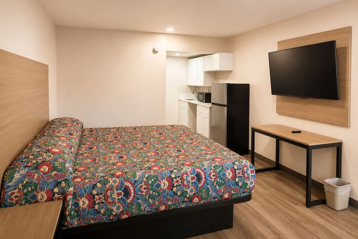 A bedroom with a bed, a small kitchenette, and a TV mounted on the wall.