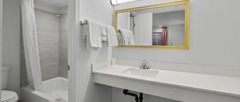 A modern bathroom with a white sink, a gold-framed mirror, and a shower area.
