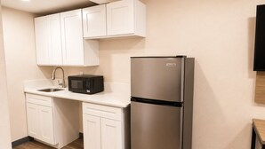 A compact kitchen with white cabinets, a stainless steel refrigerator, a microwave, and a sink. - Travel Inn - In Phoenix (Alhambra) (Phoenix)
