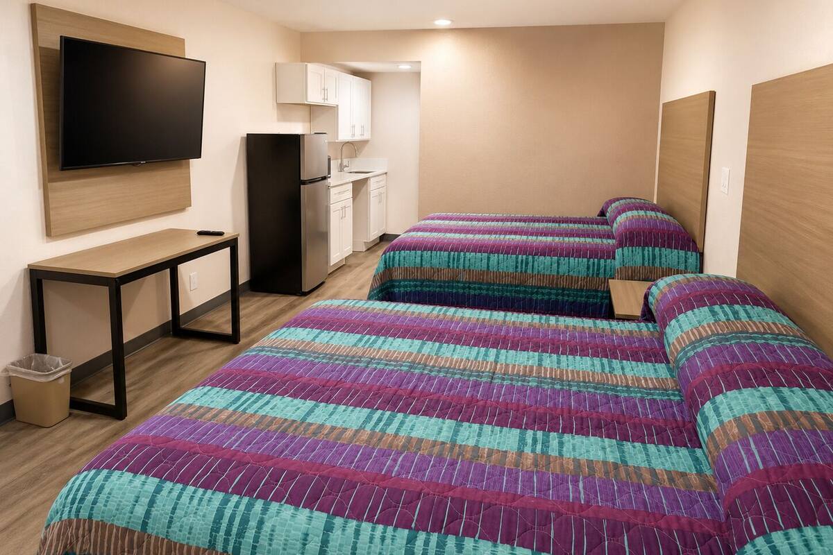 A hotel room with a bed, a desk, a TV, a mini-fridge, and a kitchenette.
