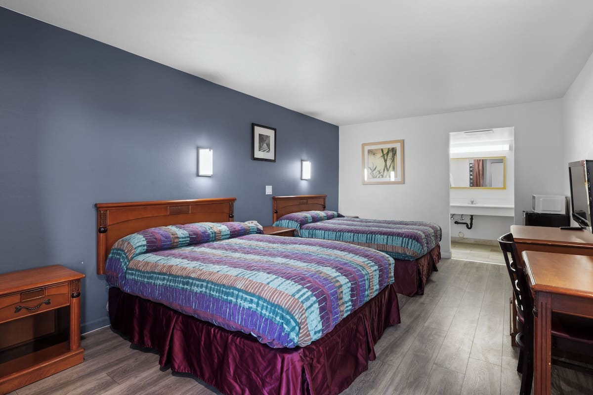 A hotel room with two beds, a wooden desk, a mirror, and a television.
