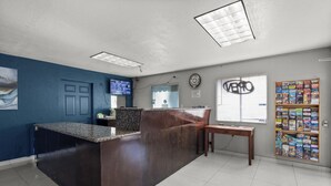 A reception area with a dark wooden counter, a blue wall, a clock, and a window with blinds. - Travel Inn - In Phoenix (Alhambra) (Phoenix)