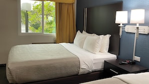 A hotel room with a large bed, a nightstand with a lamp, and a window with curtains. - Quality Inn Ontario Airport Convention Center (Ontario)
