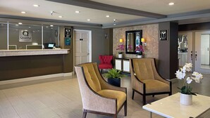 A reception area with a counter, two armchairs, a table with a vase of flowers, and a red chair. - Quality Inn Ontario Airport Convention Center (Ontario)