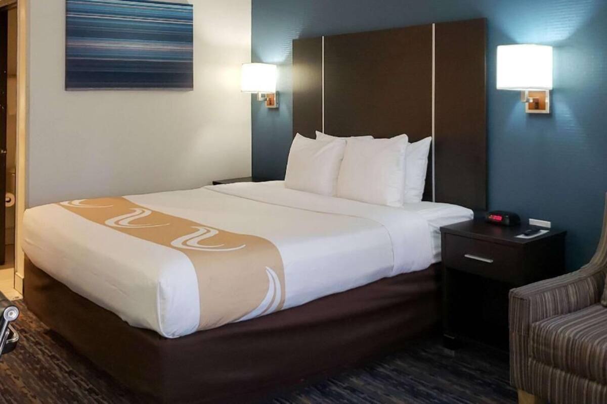 A hotel room with a large bed, two bedside tables, a chair, and a wall-mounted artwork.