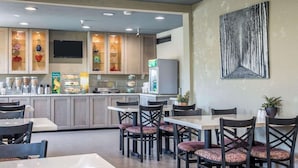 A modern kitchen with built-in appliances, a dining area with tables and chairs, and a large abstract painting on the wall. - Quality Inn Ontario Airport Convention Center (Ontario)