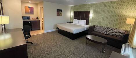 A hotel room with a bed, a sofa, a desk, a chair, a microwave, and a small kitchenette.