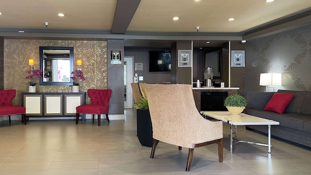 A modern hotel lobby with a reception desk, red chairs, a beige armchair, a small table with a plant, and a sofa with red cushions. - Quality Inn Ontario Airport Convention Center (Ontario)