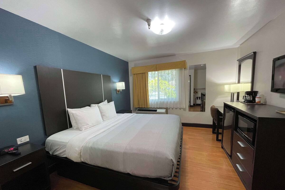 A hotel room with a bed, bedside table, desk, and a mirror.