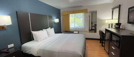 A hotel room with a bed, bedside table, desk, and a mirror.