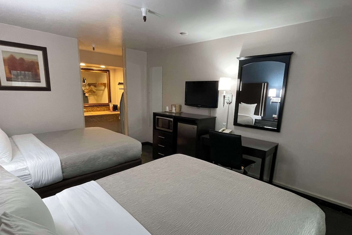 A hotel room with two beds, a desk, a TV, and a mirror.