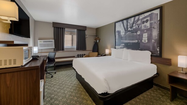 A hotel room with a large bed, a desk with a microwave, a TV, and a large window with curtains. - SureStay Hotel by Best Western Williams - Grand Canyon (Williams)