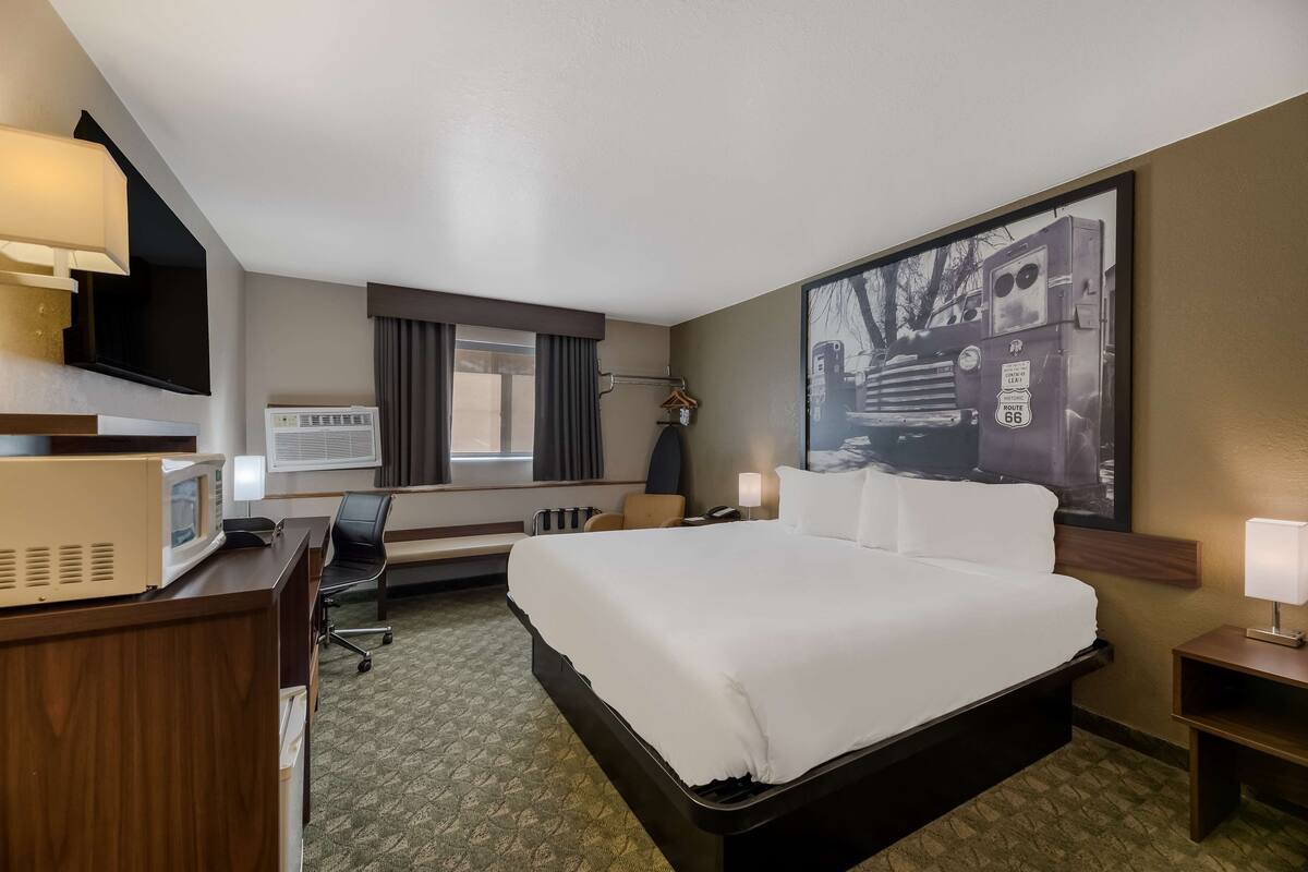 Habitación de hotel con una cama grande, un escritorio con microondas, televisor y un amplio ventanal con cortinas.