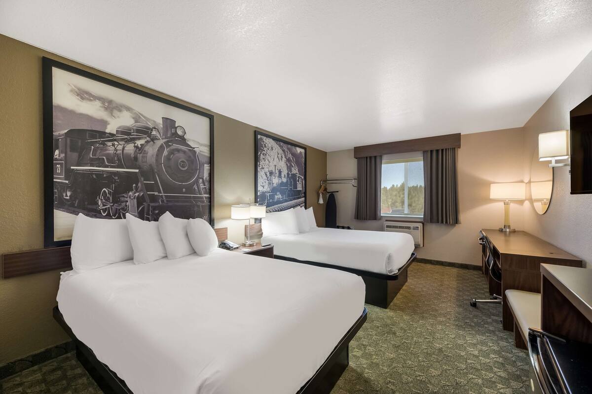 Habitación de hotel con dos camas, un escritorio, una silla, una lámpara y un cuadro grande con una imagen de un tren.