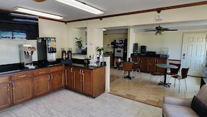 Una cocina equipada con refrigerador, cafetera y microondas. Hay un comedor con sillas y una mesa.
