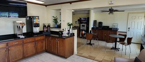 A kitchen with a refrigerator, coffee machine, and microwave. There is a dining area with chairs and a table.