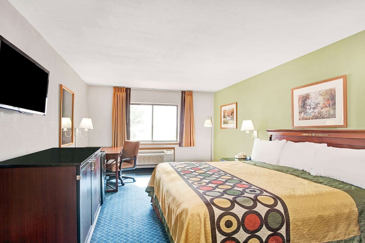 A hotel room with a bed, desk, chair, TV, and artwork on the walls.