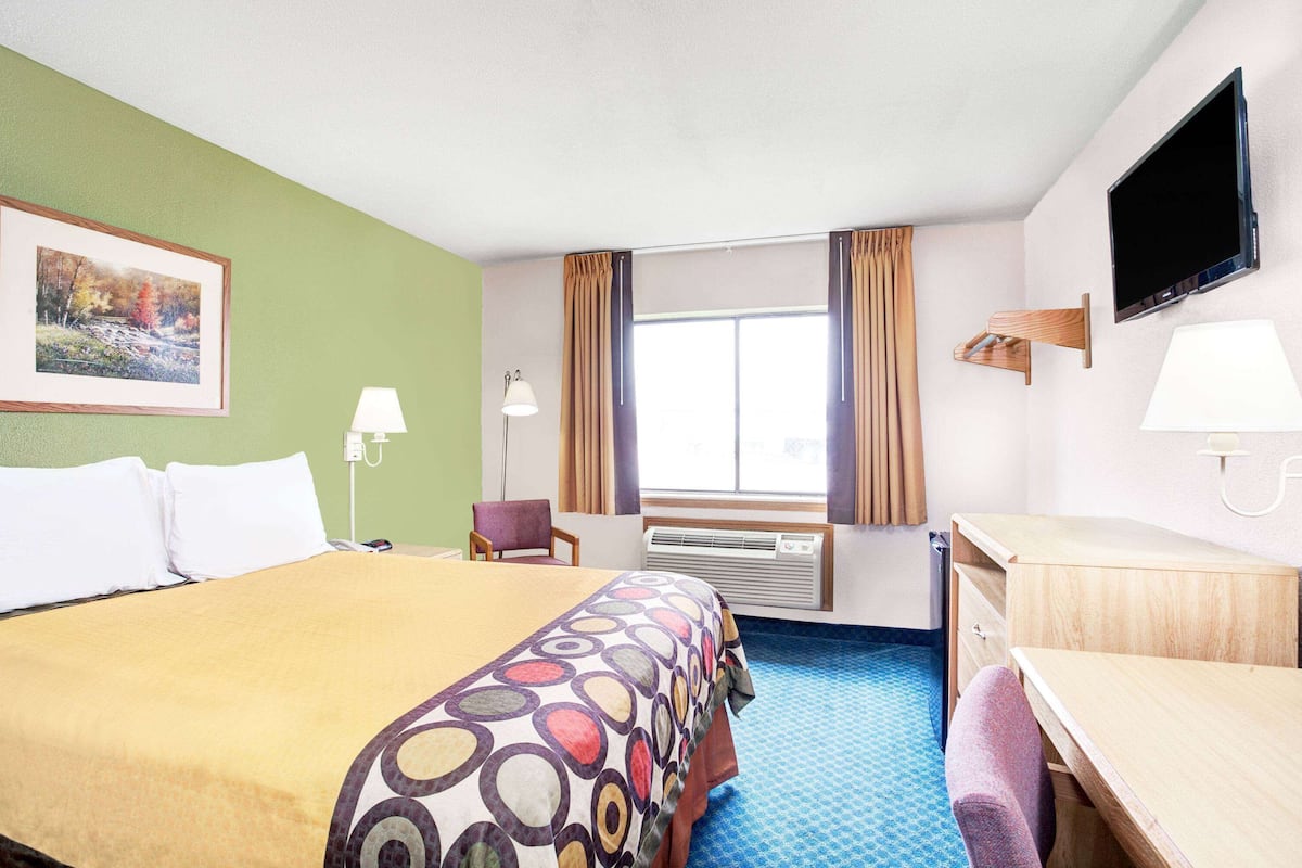 A hotel room with a bed, a desk, a chair, a TV, and a window with curtains.