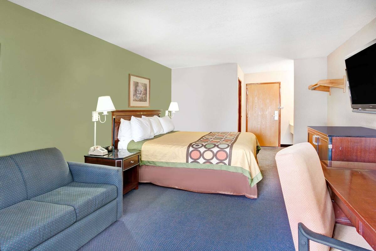 A hotel room with a bed, a desk, a chair, a sofa, and a TV.