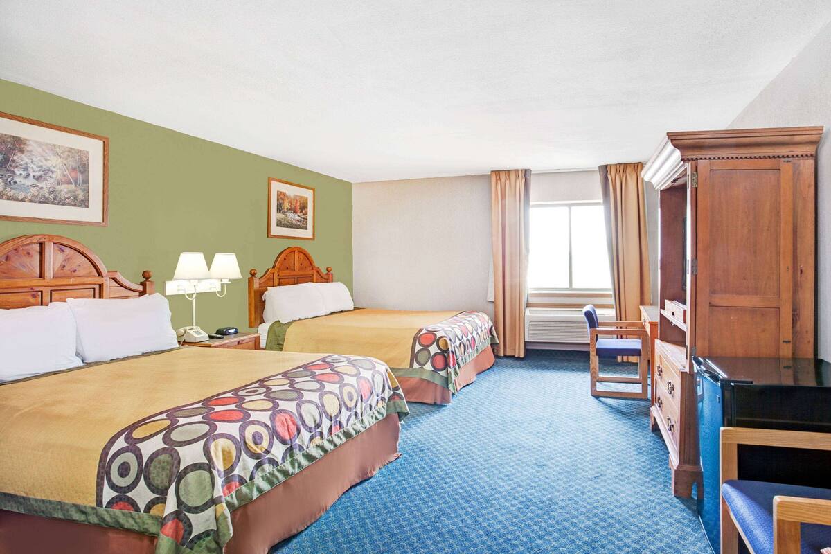 A hotel room with two beds, a desk, a chair, a dresser, and a large window with curtains.