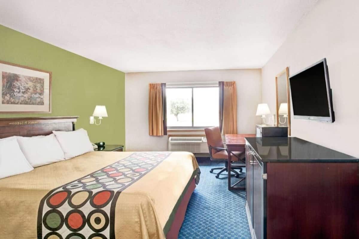 A hotel room with a bed, desk, chair, television, and a window with curtains.