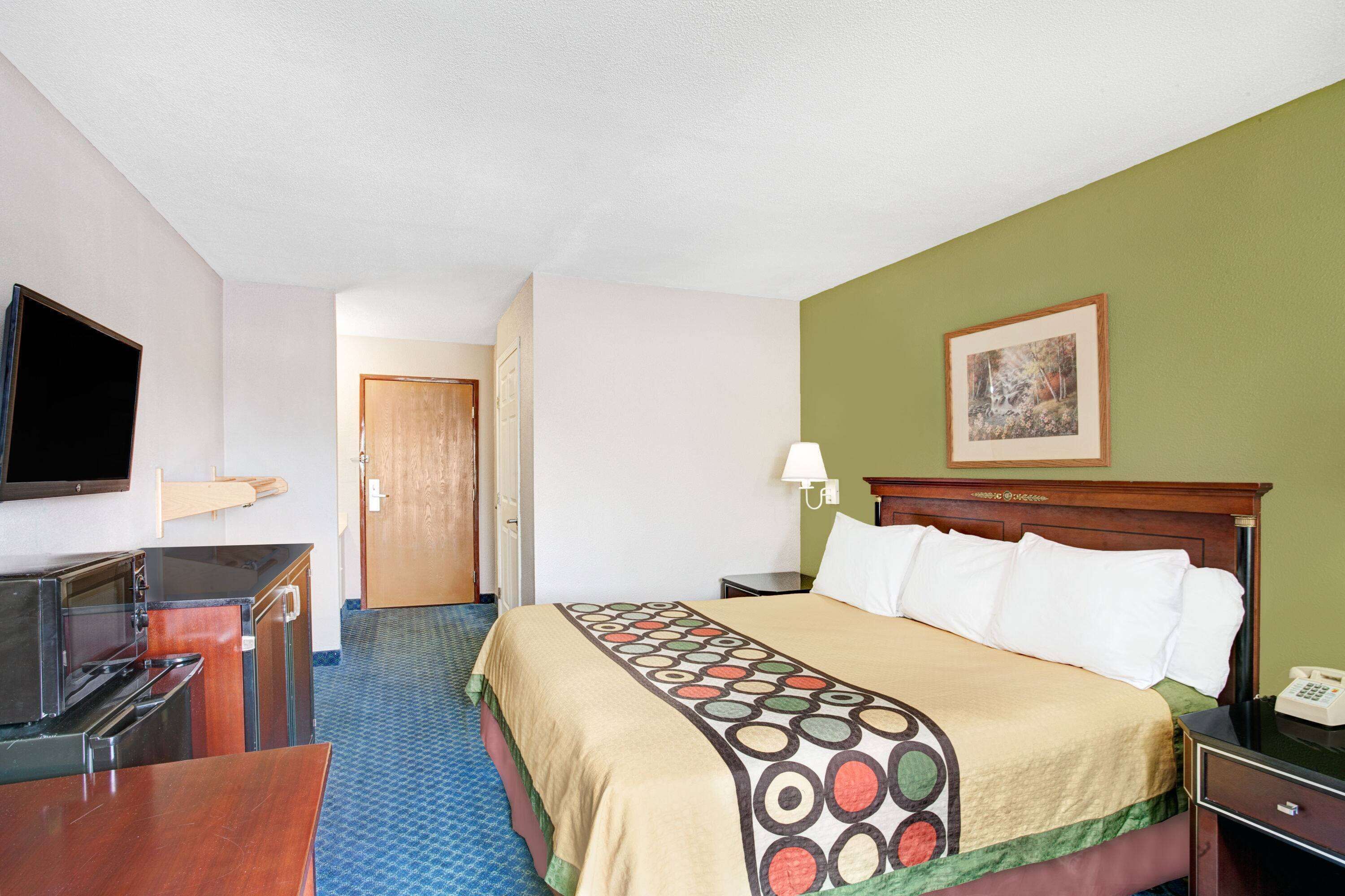 A hotel room with a bed, a TV, a desk, and a telephone.