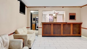 Un amplio espacio de sala con un sofá color beige, un mueble de entretenimiento de madera y una cocina al fondo.