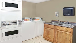 Una cocina con microondas, dos lavadoras, un lavabo y dispensador de jabón.