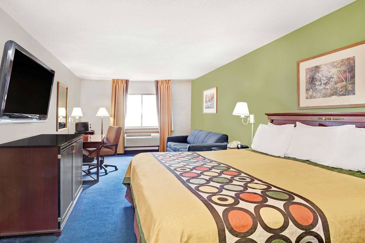 A hotel room with a bed, a desk, a chair, a television, and a window with curtains.