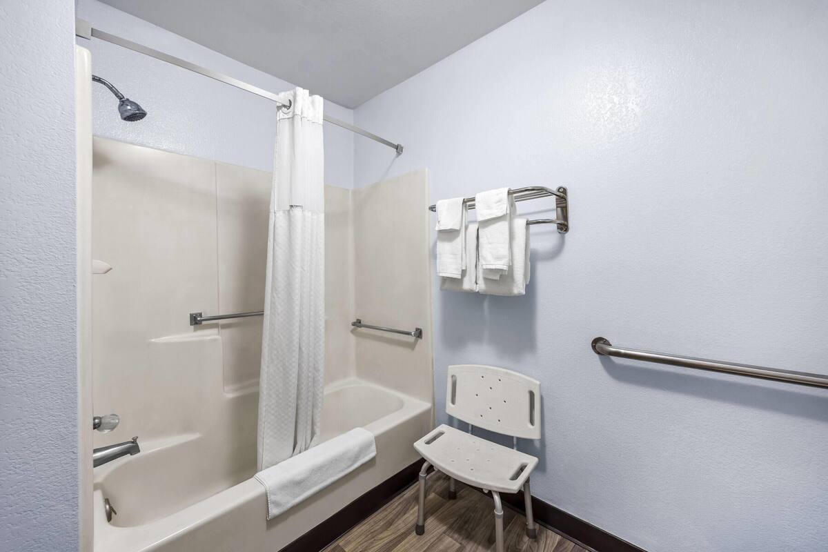 Ein Badezimmer mit Badewanne, Dusche, einer Haltestange und einer rollstuhlgerechten Sitzbank.